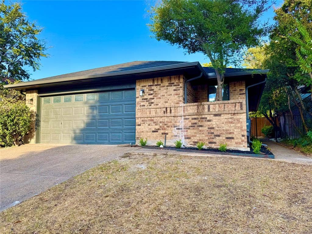 3706 Aries Drive, Garland, TX 75044 Brick exterior with a dark-paneled garage door, mature trees, and a concrete driveway