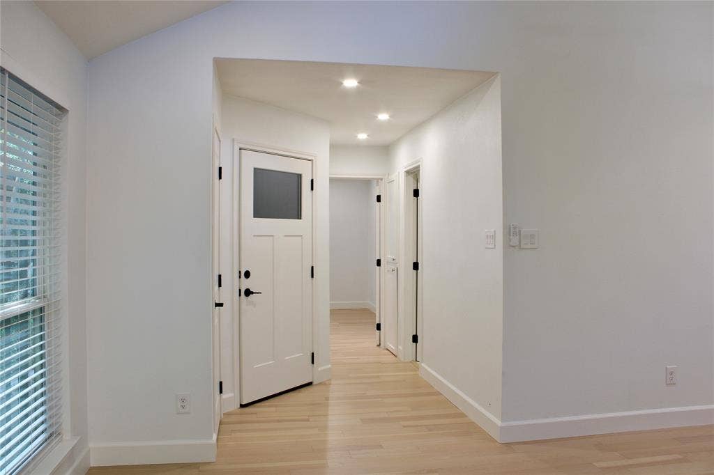 3706 Aries Drive, Garland, TX 75044 Recessed lighting illuminates the hallway, featuring light wood-finish flooring and multiple white paneled doors with matte black hardware