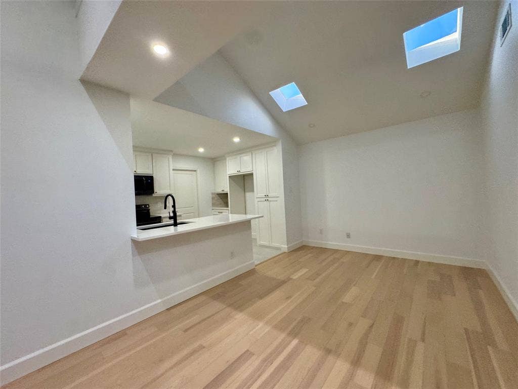 3706 Aries Drive, Garland, TX 75044 Vaulted ceiling with multiple skylights, recessed lighting, wood-finish flooring, and a kitchen featuring white cabinetry, a black faucet, and built-in appliances