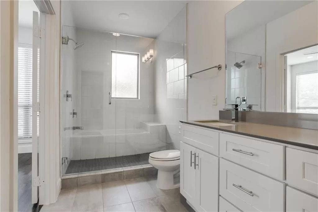 4303 Cole Avenue, #17, Dallas, TX 75205 Spacious bathroom featuring a glass-enclosed shower, white vanity with ample storage, integrated sink, and large wall-mounted mirror
