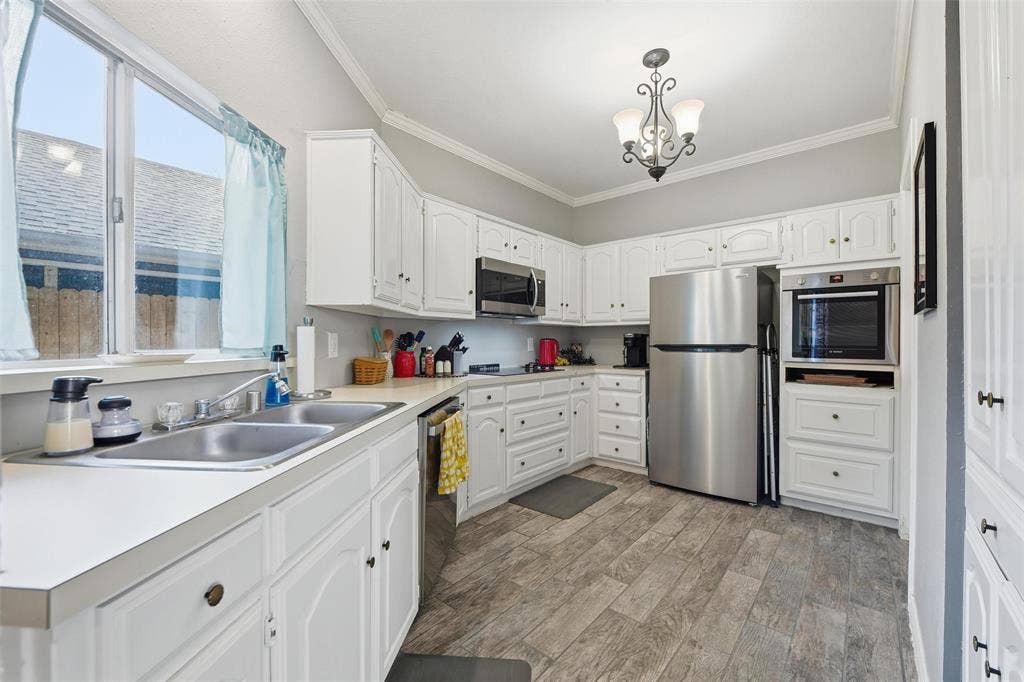 White cabinetry with dark hardware, stainless steel appliances, wood-finish flooring, dual-basin stainless steel sink, and a built-in oven