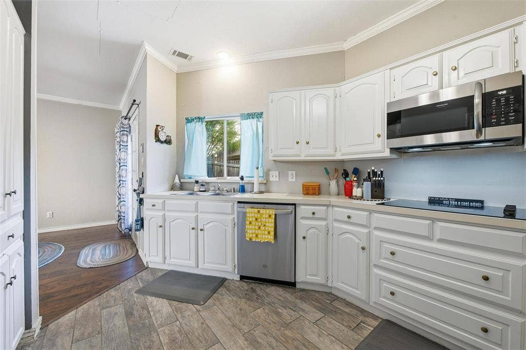 White cabinetry and countertops with stainless steel appliances, including an over-the-range microwave, dishwasher, and electric cooktop