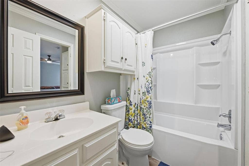 White vanity with integrated sink, framed mirror, built-in upper cabinetry, and a shower-tub combination with shelving