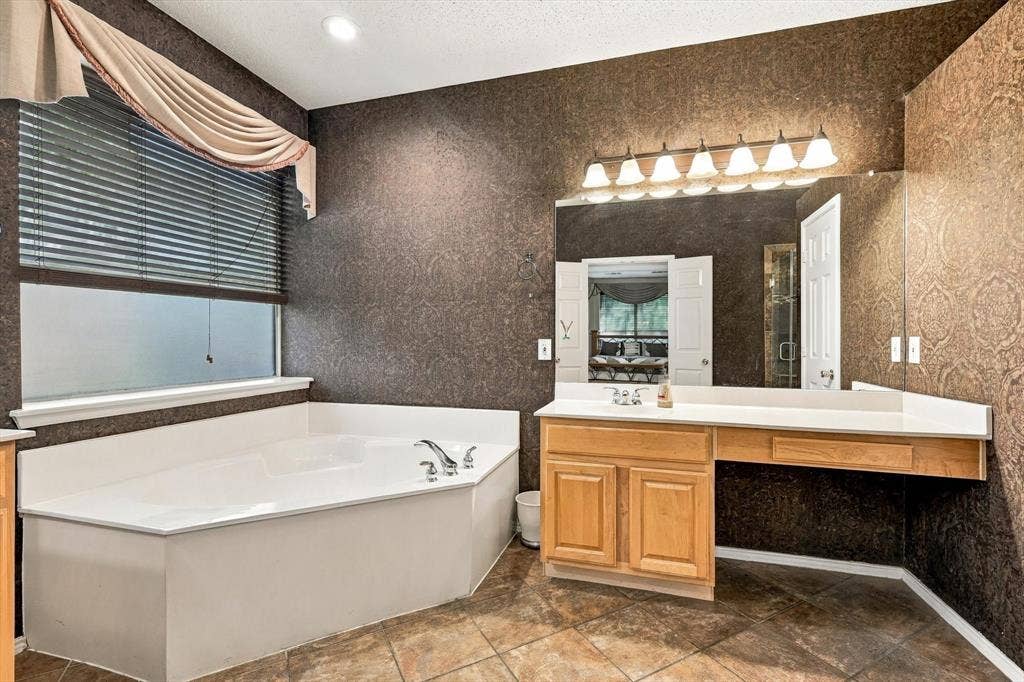 103 Deerpath Road, Hickory Creek, TX 75065 Corner soaking tub with deck-mounted fixtures, wood-finish vanity with countertop, large wall-mounted mirror, and tile flooring