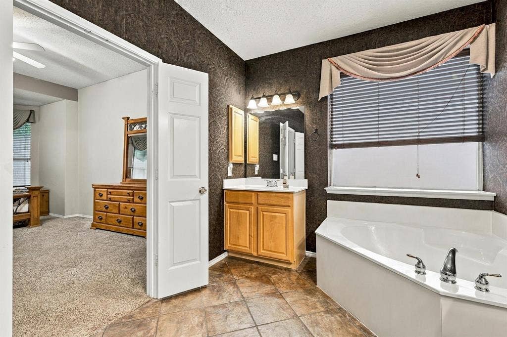 103 Deerpath Road, Hickory Creek, TX 75065 Bathroom featuring a built-in corner soaking tub, a single vanity with wood-finish cabinetry, and patterned wall covering