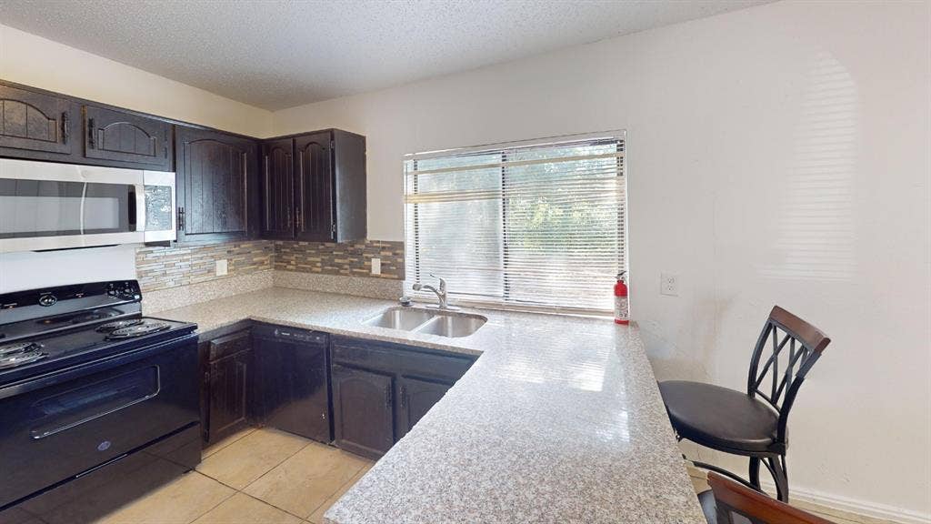 1710 Meridian Way, Garland, TX 75040 U-shaped counter with a dual basin sink, stainless steel microwave, black electric range, and dark wood-finish cabinetry