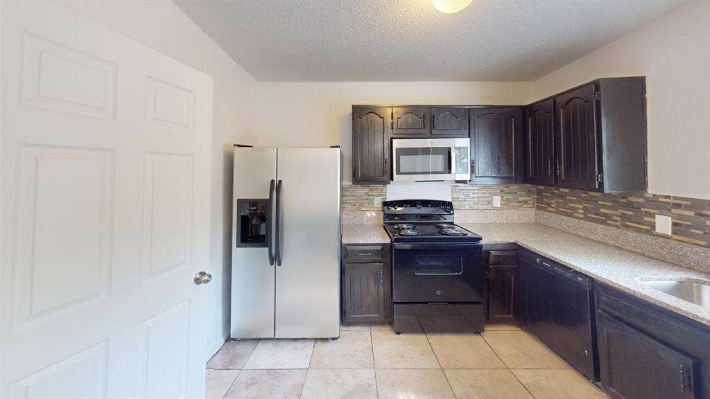 1710 Meridian Way, Garland, TX 75040 Kitchen featuring dark wood cabinetry, light-toned countertops, a mosaic tile backsplash, a stainless steel refrigerator, and a built-in microwave