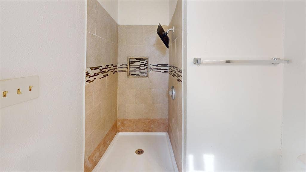 1710 Meridian Way, Garland, TX 75040 Tiled shower stall featuring a built-in niche, decorative accent band, and a single-handle shower fixture