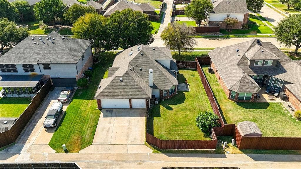 Pitched shingle roof, attached two-car garage, concrete driveway, fenced backyard, and a small outbuilding