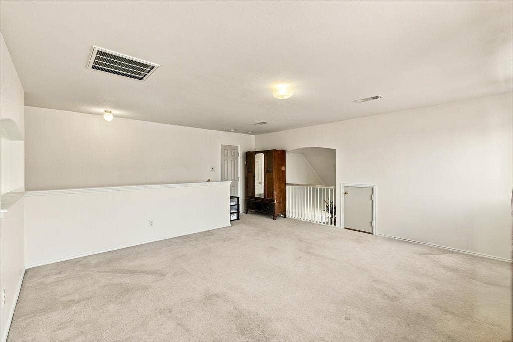 Expansive carpeted area with white walls, recessed ceiling lighting, and a white half-wall railing