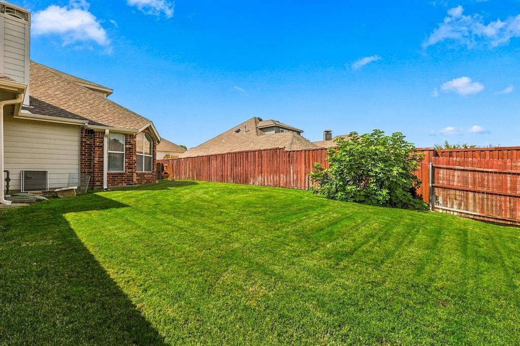 Expansive rear yard featuring green lawn, a privacy fence, and mature landscaping