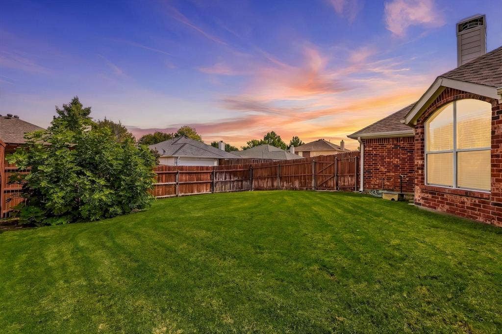Expansive green lawn, wood fence, brick exterior, arched window, and a prominent chimney