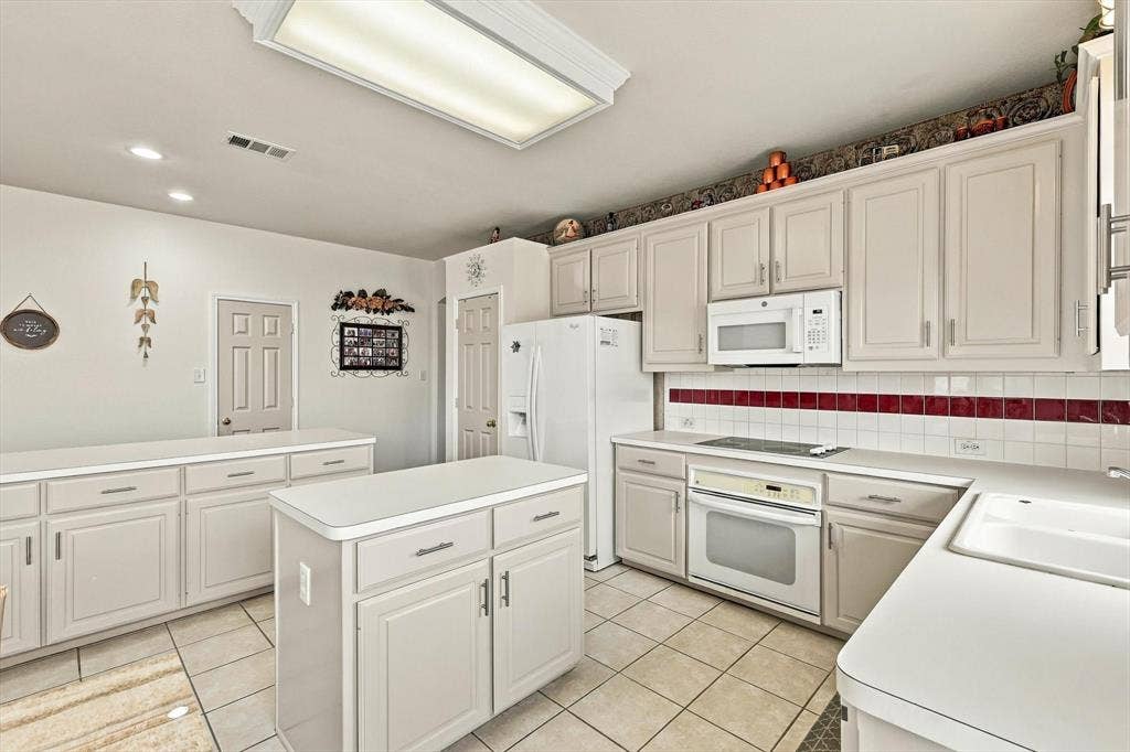 White cabinetry with brushed nickel hardware, expansive counter space, integrated white appliances, and ceramic tile flooring