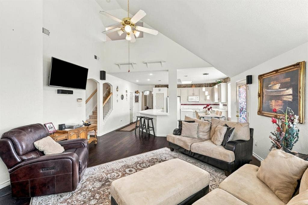 Vaulted ceiling with ceiling fan, wood-finish flooring, white walls, arched doorway, and staircase with wood handrail
