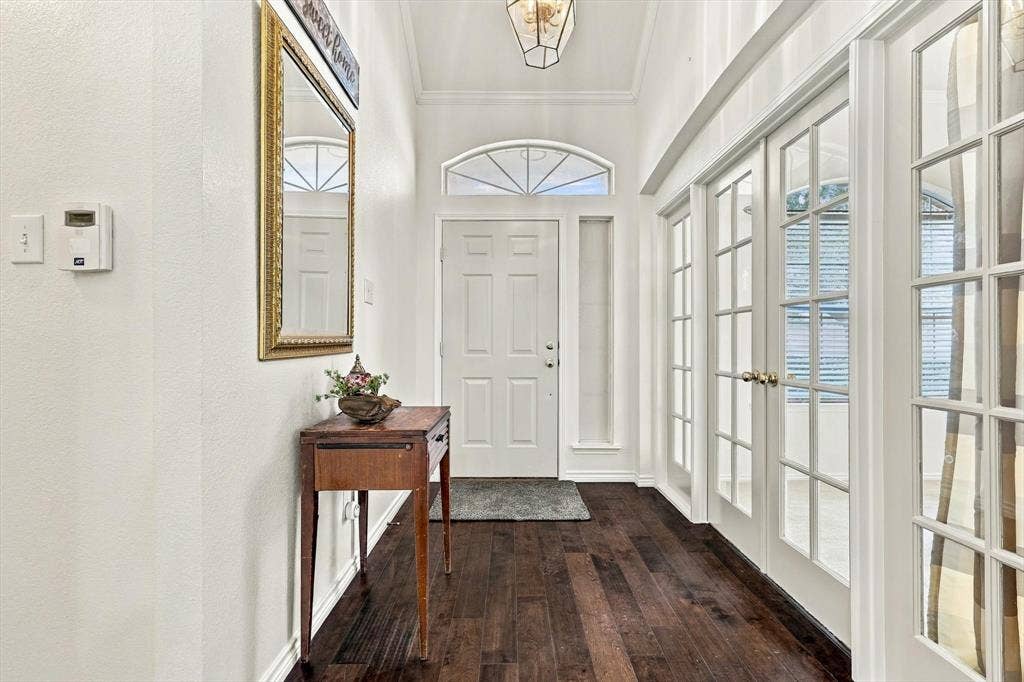 Wood-finish flooring, white paneled walls, a vaulted ceiling, a transom window above the entry door, and double French doors