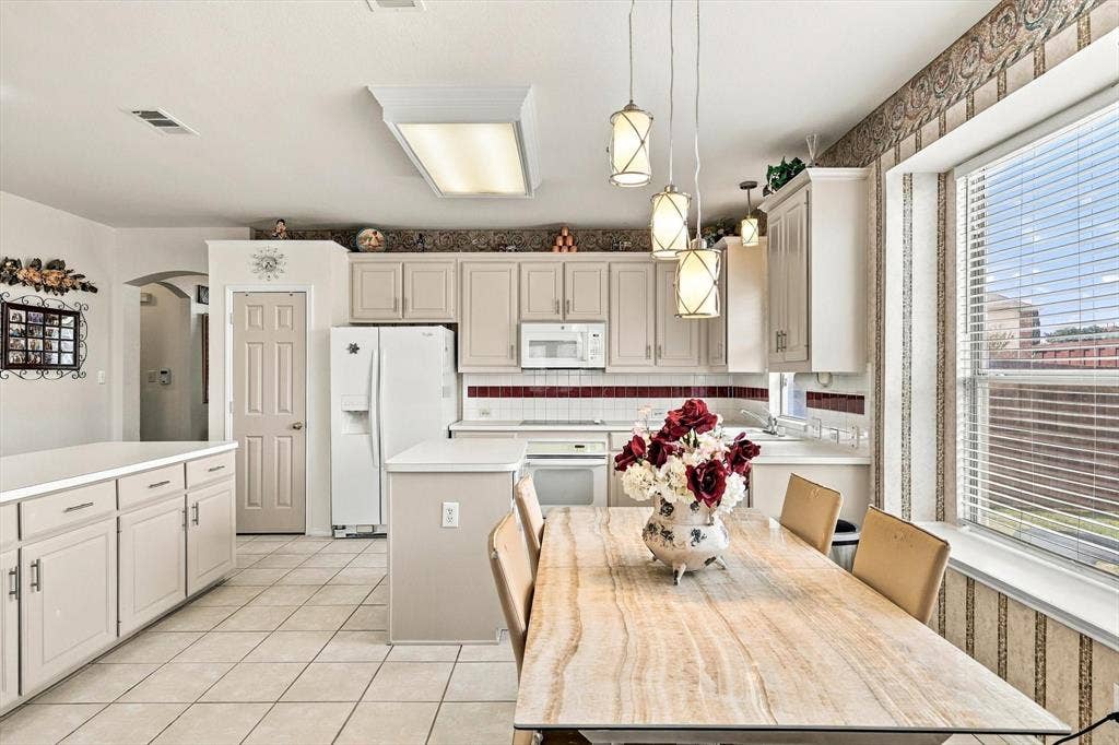 Tile flooring, white cabinetry, white appliances, pendant lighting, and a kitchen island
