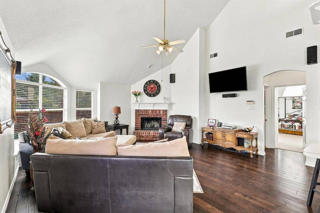 Vaulted ceilings, wood-finish flooring, brick-surround fireplace, arched window, and ceiling fan