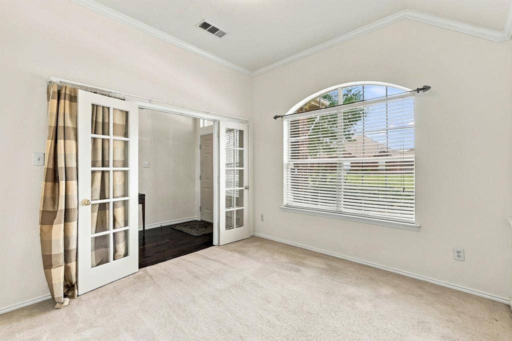 Arched window with blinds, French doors with glass panels, crown molding, and carpet flooring