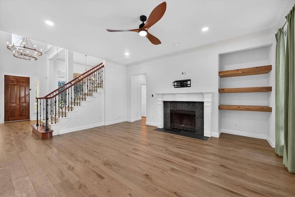 10601 Whispering Pines Drive, Frisco, TX 75033 Hardwood-style flooring throughout, featuring a fireplace with a stone surround and white mantel, built-in shelving with wood accents, and a staircase with an ornamental iron railing