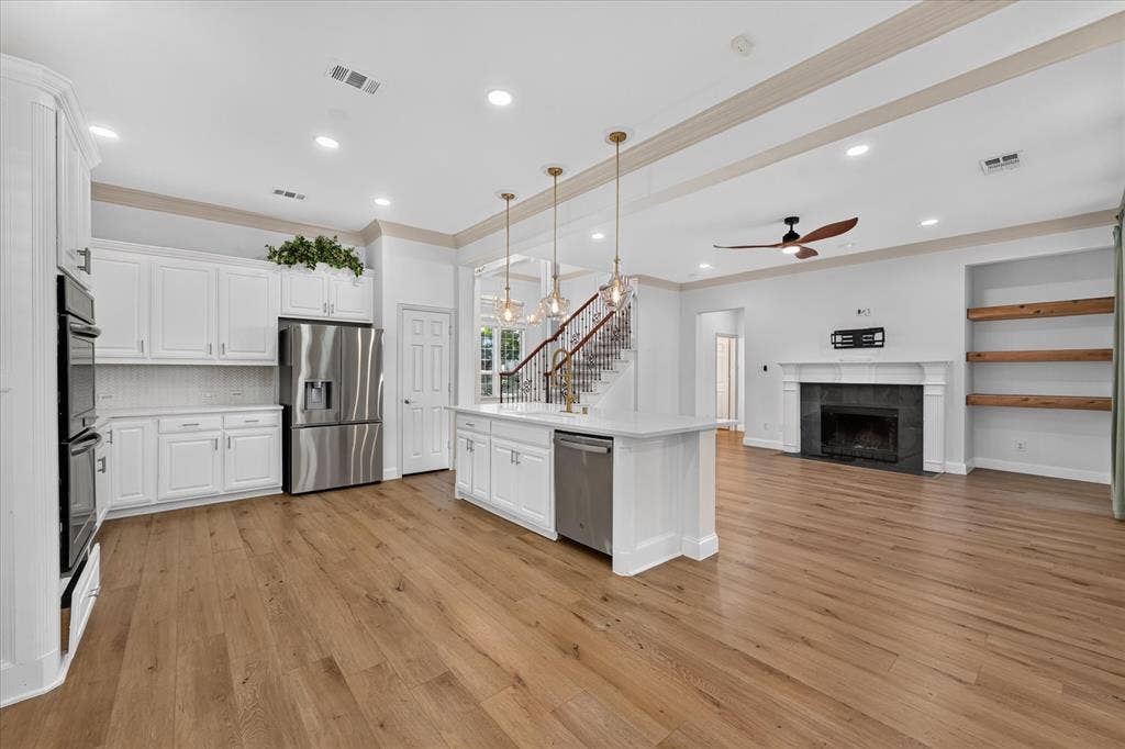 10601 Whispering Pines Drive, Frisco, TX 75033 White shaker cabinetry, stainless steel appliances, wood-finish flooring, built-in fireplace, and integrated shelving