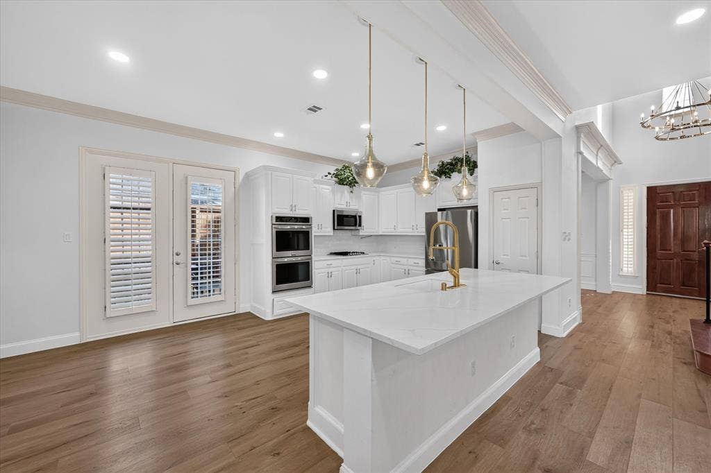 10601 Whispering Pines Drive, Frisco, TX 75033 Kitchen featuring a large island with a gold-tone faucet, white cabinetry, built-in double ovens, and wood-finish flooring