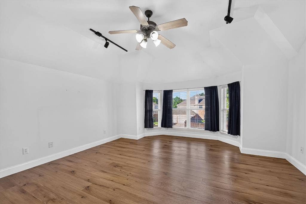 10601 Whispering Pines Drive, Frisco, TX 75033 Bay window with custom treatments, wood-finish flooring, vaulted ceiling, ceiling fan with integrated lighting, and track lighting