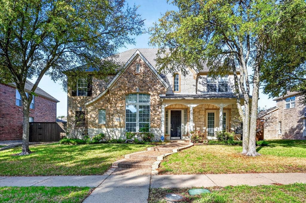 10601 Whispering Pines Drive, Frisco, TX 75033 Stone and brick exterior with a pitched roof, featuring a covered front porch with arched openings and columns