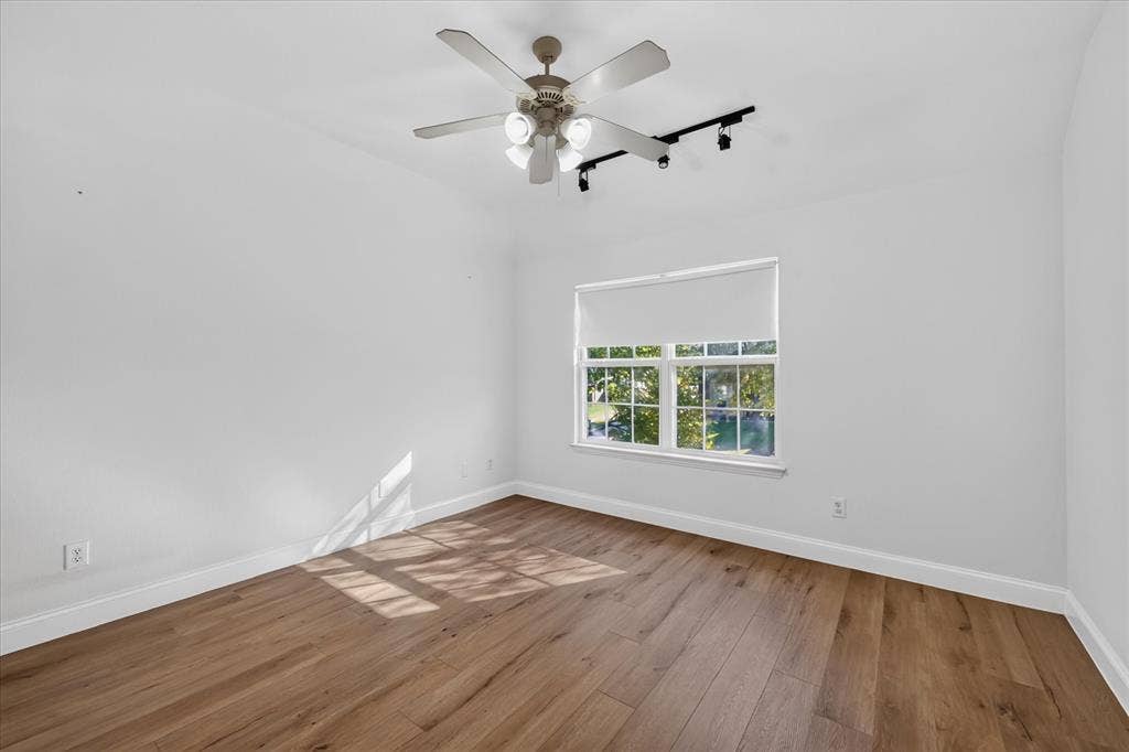 10601 Whispering Pines Drive, Frisco, TX 75033 Wood-finish flooring, white walls, window with roller shade, ceiling fan, and track lighting fixture