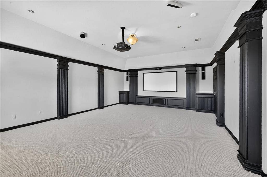 10601 Whispering Pines Drive, Frisco, TX 75033 Dedicated media room featuring recessed ceiling lighting, a ceiling-mounted projector, built-in cabinetry with display shelving, large projection screen, black architectural framing elements, and neutral carpet flooring throughout