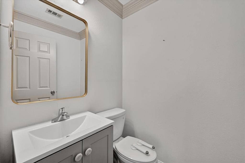 10601 Whispering Pines Drive, Frisco, TX 75033 Vanity with an integrated sink, polished chrome faucet, rectangular gold-framed mirror, and a toilet