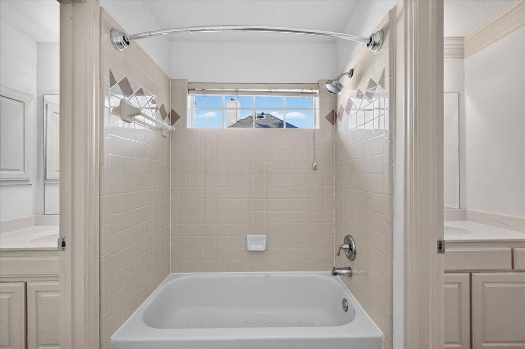 10601 Whispering Pines Drive, Frisco, TX 75033 Bathtub and shower combination with tiled surround, decorative accent tiling, a window, and chrome fixtures