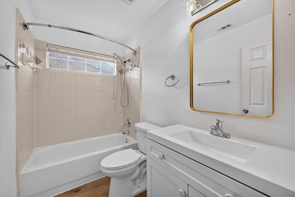 10601 Whispering Pines Drive, Frisco, TX 75033 White vanity with integrated sink, rectangular gold-framed mirror, wood-finish flooring, and a shower-tub combination with light-toned wall tile