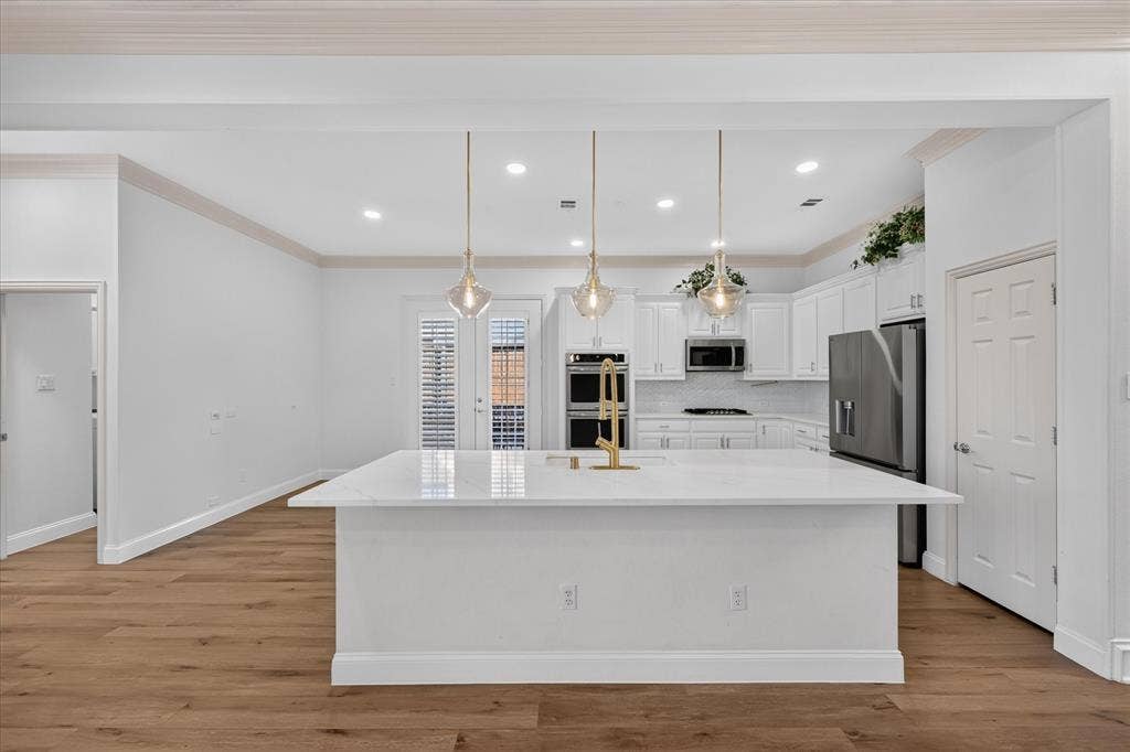 10601 Whispering Pines Drive, Frisco, TX 75033 Gourmet kitchen featuring a large island with white stone countertop, white cabinetry, integrated stainless steel appliances, and wood-finish flooring