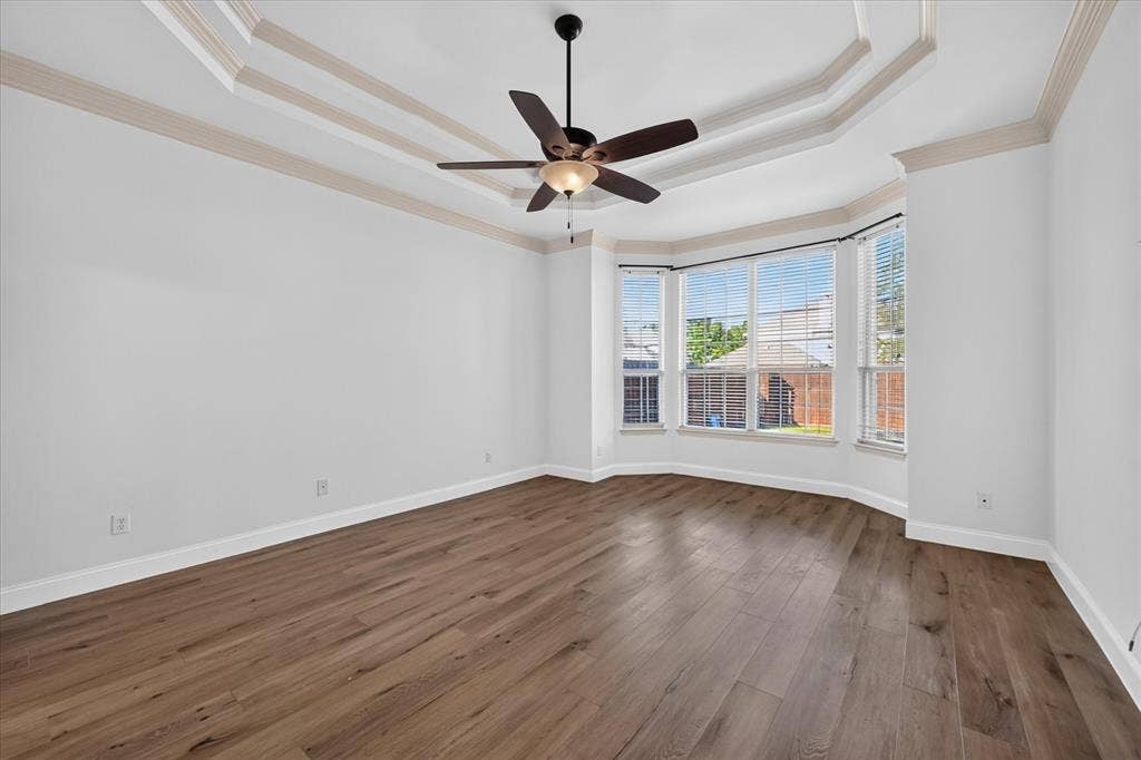 10601 Whispering Pines Drive, Frisco, TX 75033 Tray ceiling with decorative molding, wood-finish flooring, bay windows, and a ceiling fan with integrated lighting