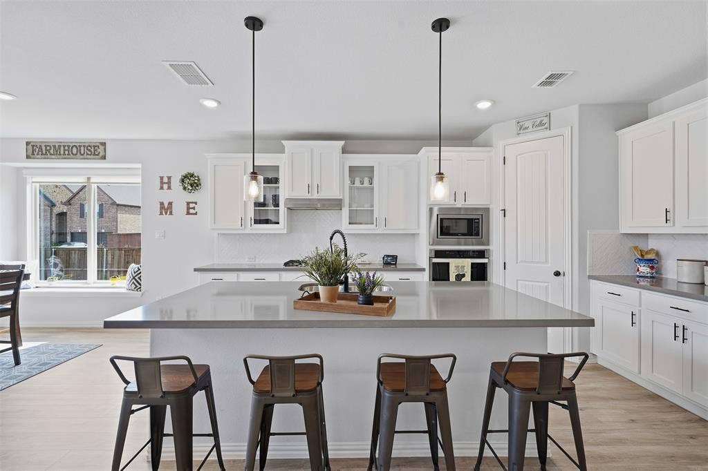 Kitchen featuring a large island with pendant lighting, white cabinetry, integrated stainless steel microwave, and wood-finish flooring