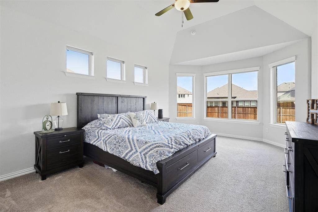 Vaulted ceiling with a ceiling fan, bay window configuration, high transom windows, and carpet flooring