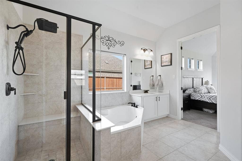Shower enclosure with black framing and built-in bench, corner soaking tub, single vanity with white cabinetry, wall-mounted light fixture, and tiled flooring