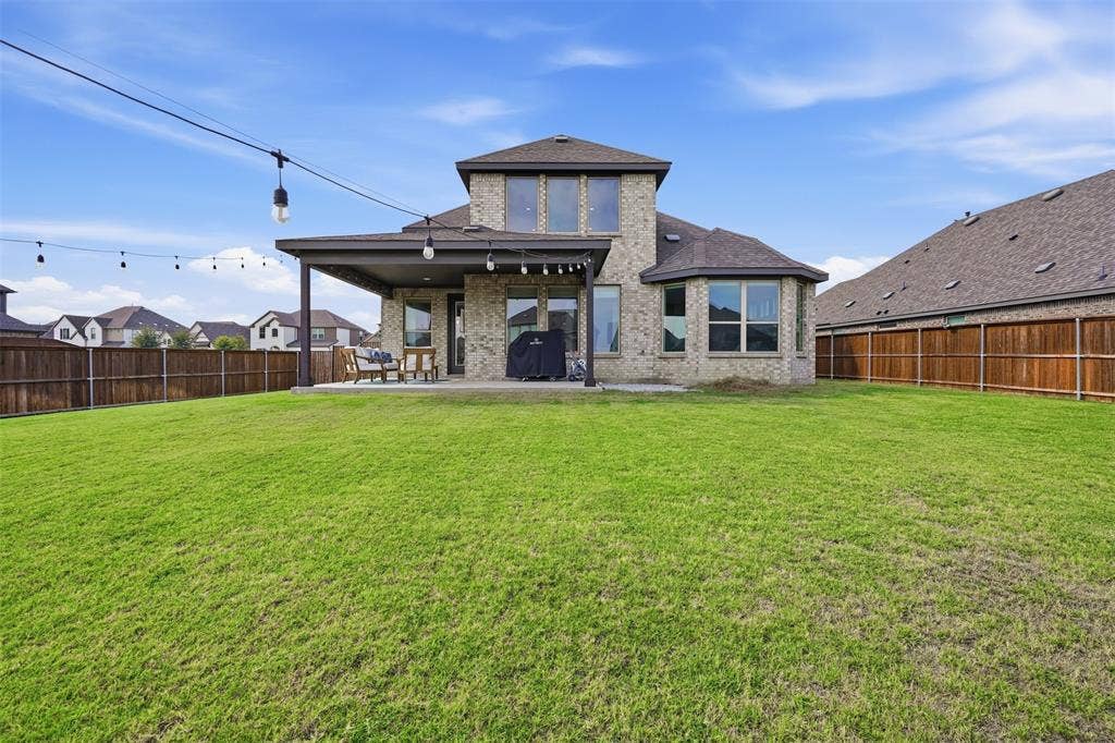 Expansive green lawn with a covered patio, string lighting, and a wood privacy fence