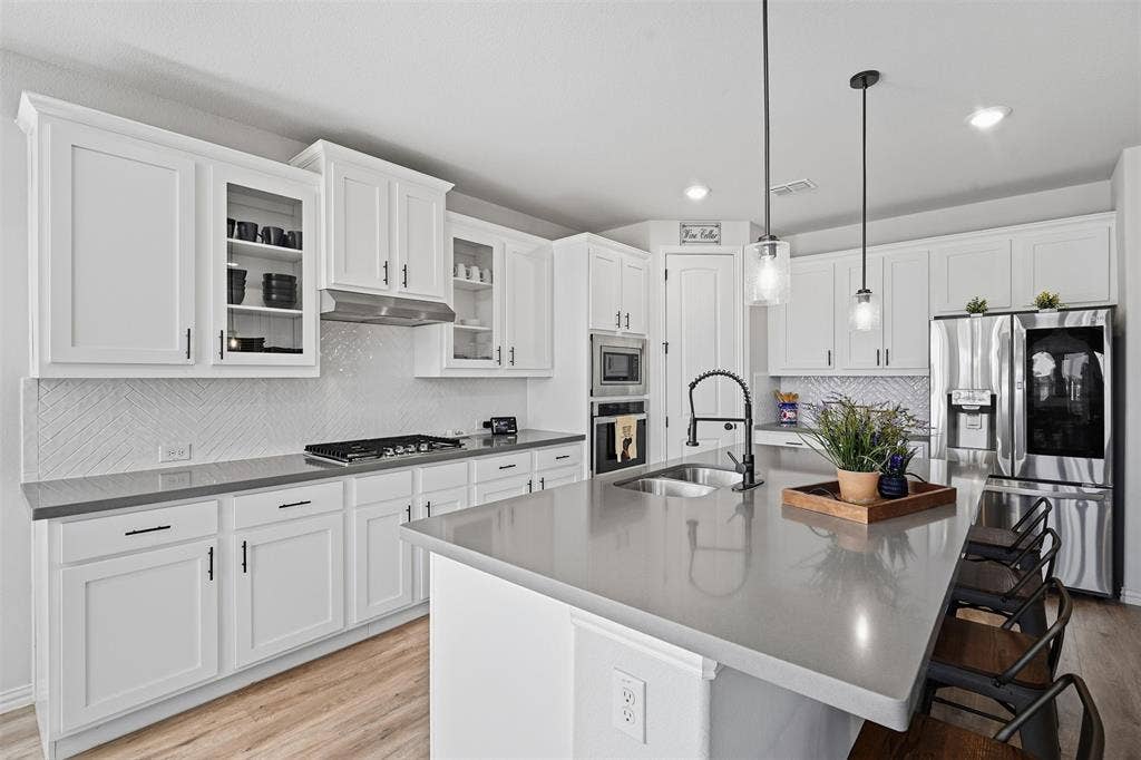 Kitchen featuring white shaker cabinetry, stainless steel appliances, a large center island with a sink, pendant lighting, and wood-finish flooring