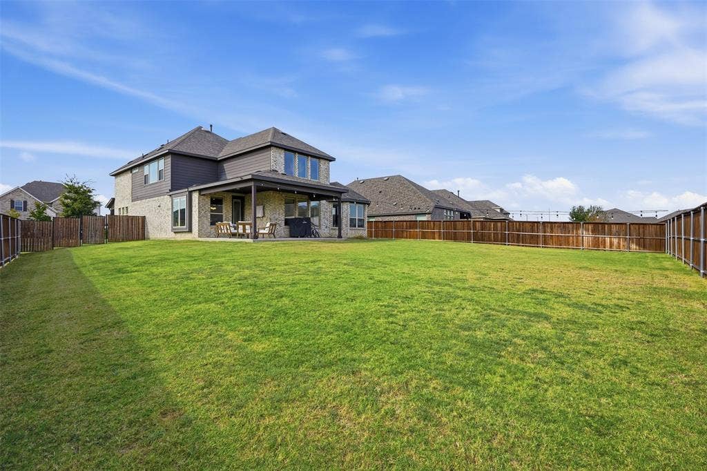 Expansive backyard with a covered patio, wood privacy fencing, and a two-story residence with brick and siding exterior