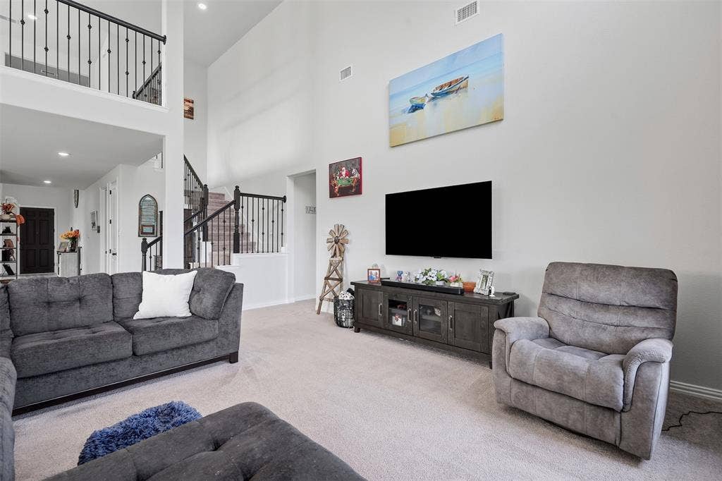Two-story living area with high ceilings, carpeted flooring, and a media console