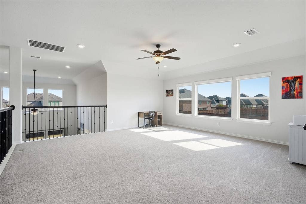 Spacious carpeted room featuring a ceiling fan, recessed lighting, and multiple windows