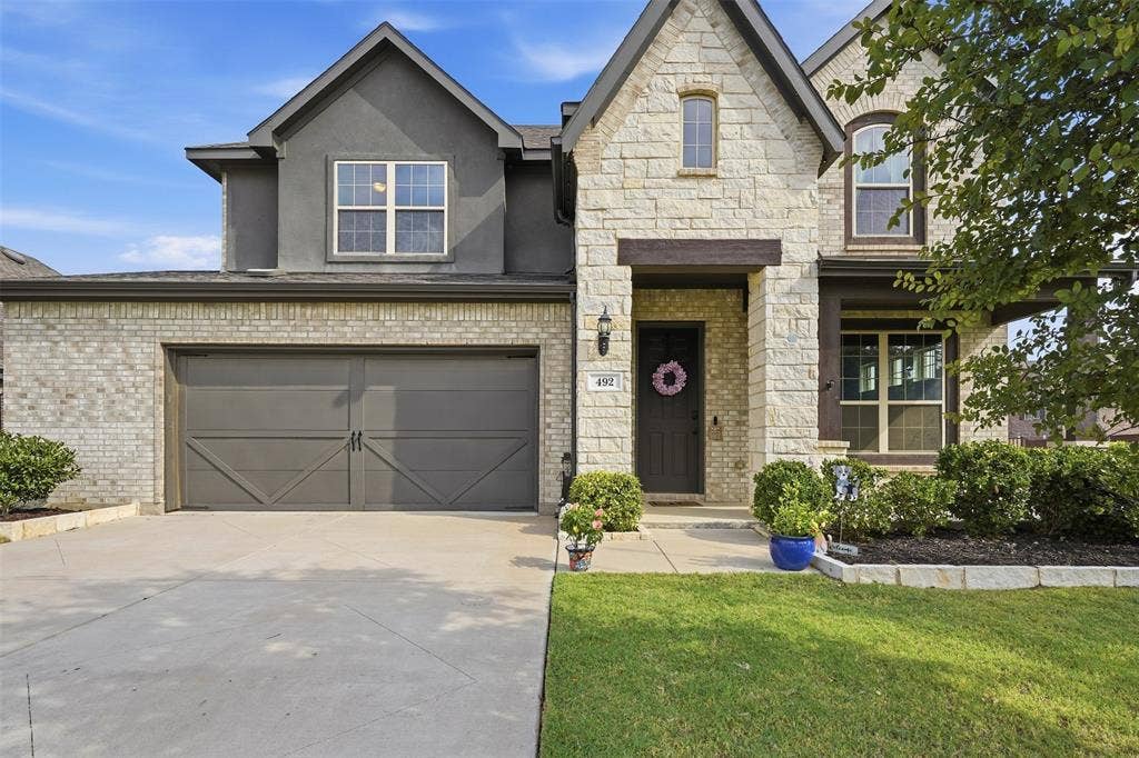 Stone and brick facade with stucco accents, an attached two-car garage, concrete driveway, and front lawn