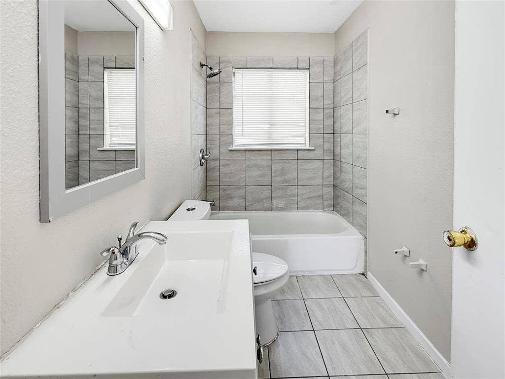 Bathroom featuring a white vanity with integrated sink, chrome faucet, framed mirror, and tiled shower surround with bathtub
