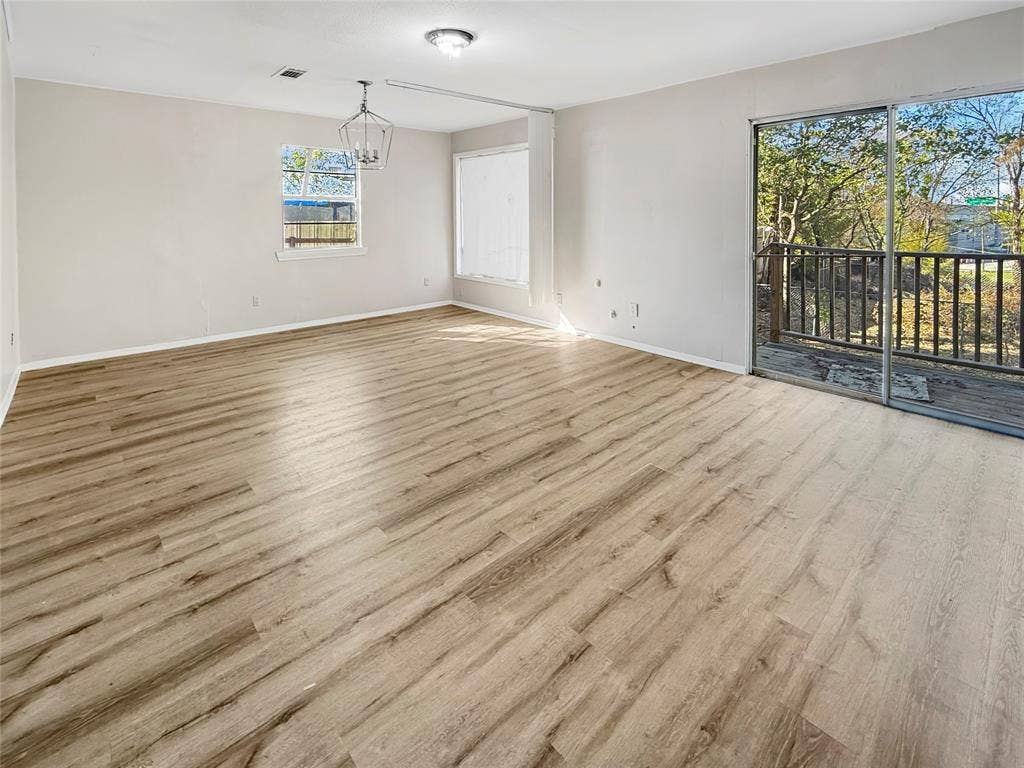 Spacious room featuring wood-finish flooring, a contemporary chandelier, a sliding glass door to an outdoor deck, and a window for natural light