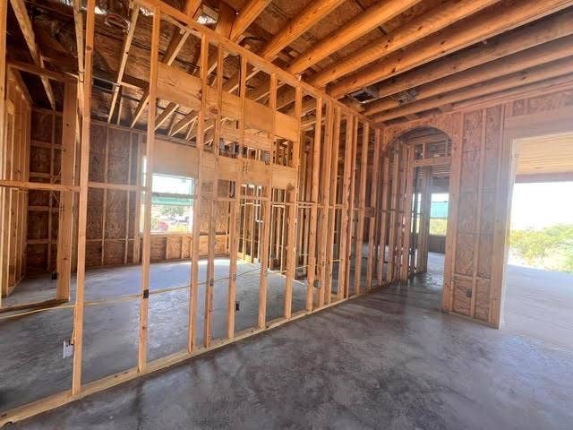 816 Oak Lane, Cottonwood Shores, TX 78657 Open framing construction with exposed ceiling joists, concrete slab foundation, and an arched doorway. Looking from the living room toward the primary bedroom