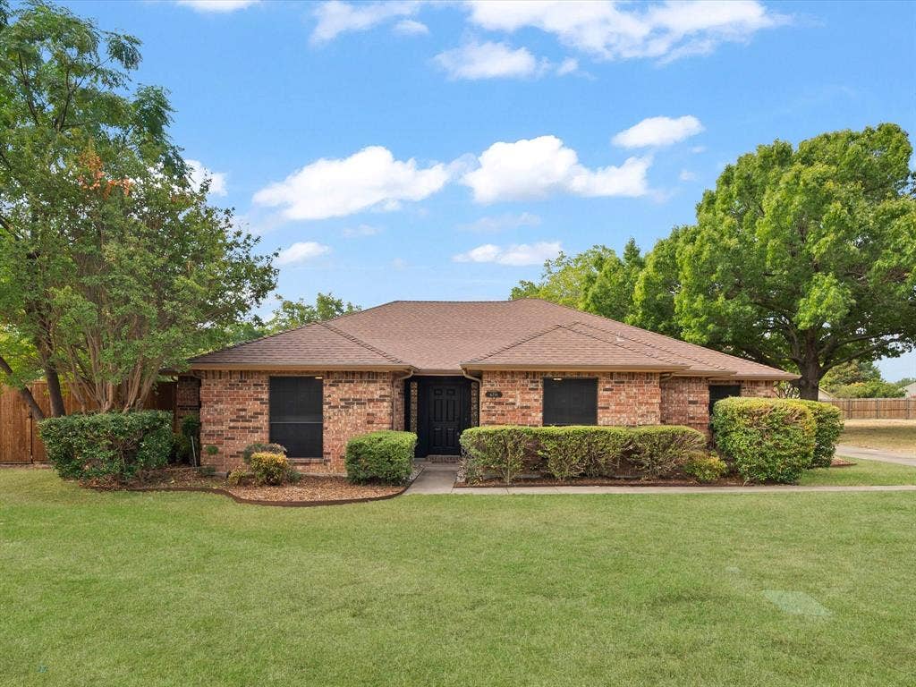 Brick exterior with a brown shingle roof, mature landscaping, and a manicured lawn
