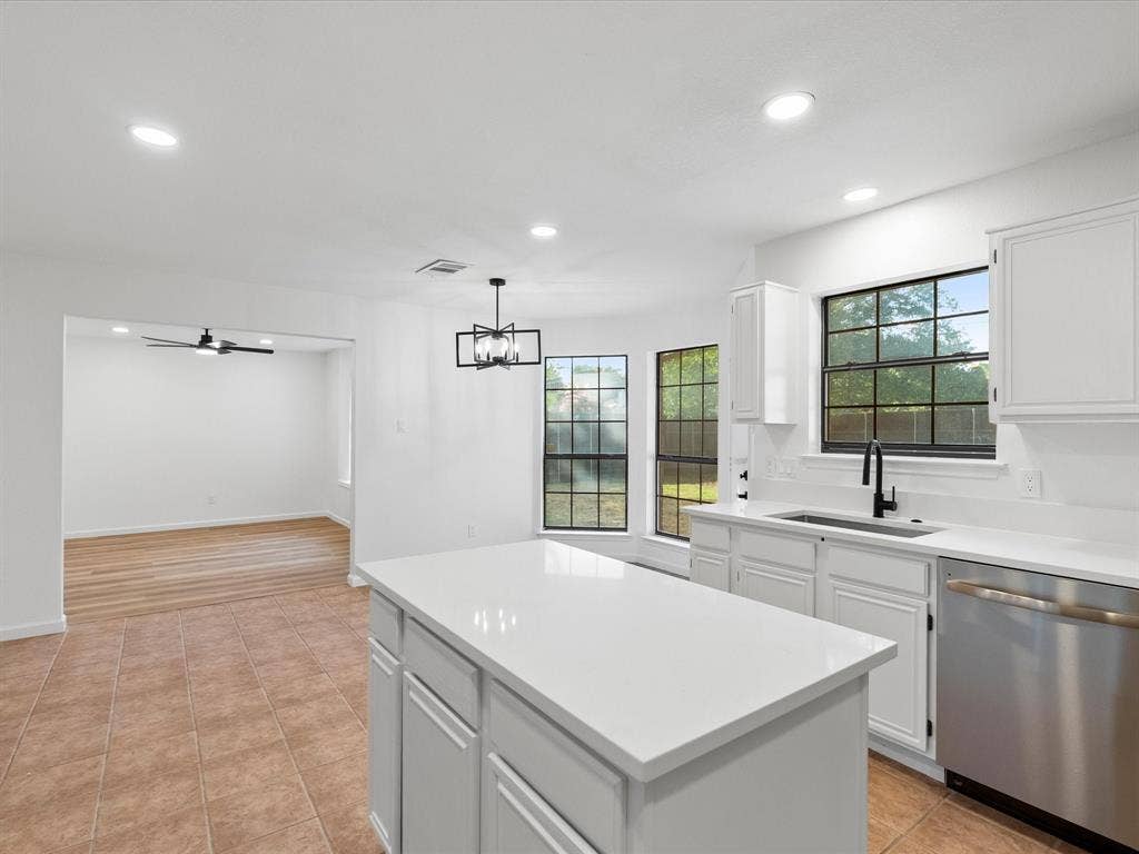 Kitchen featuring a white countertop island, stainless steel dishwasher, white cabinetry, and a black-framed window