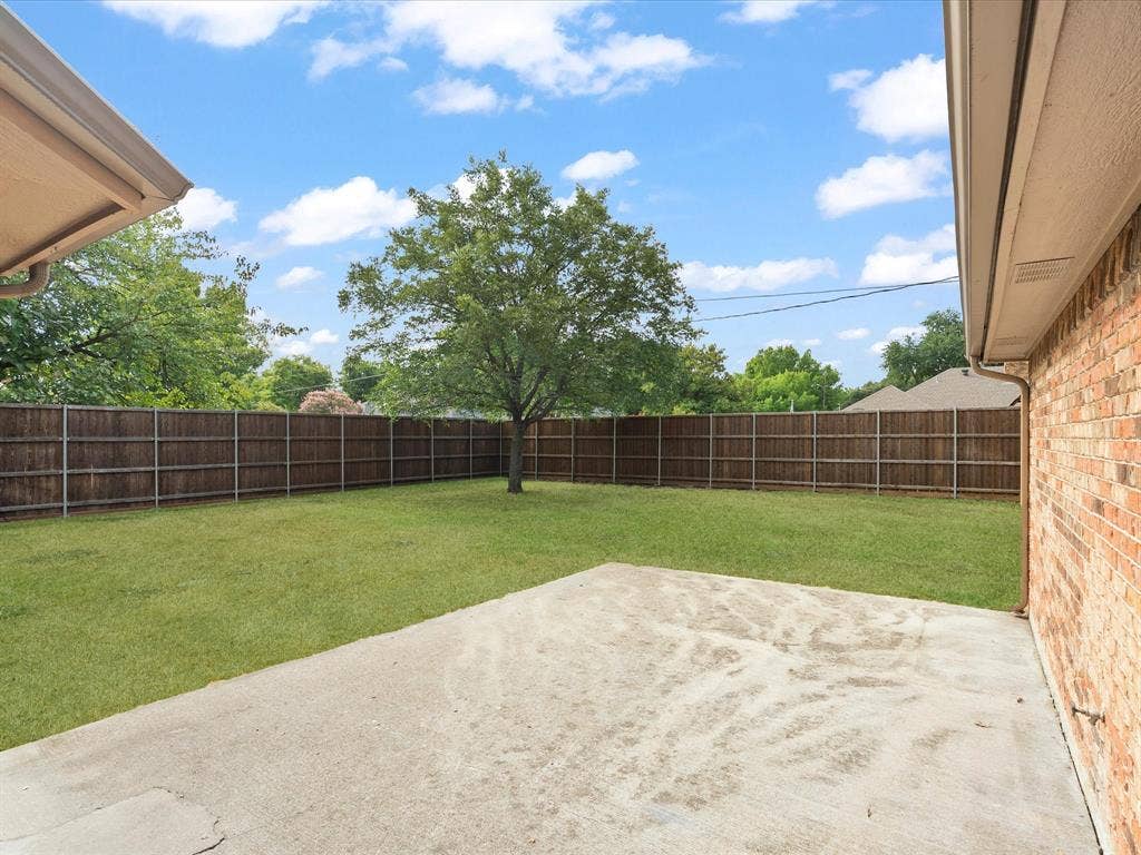 Expansive grass lawn with a mature shade tree, full privacy fencing, and a concrete patio