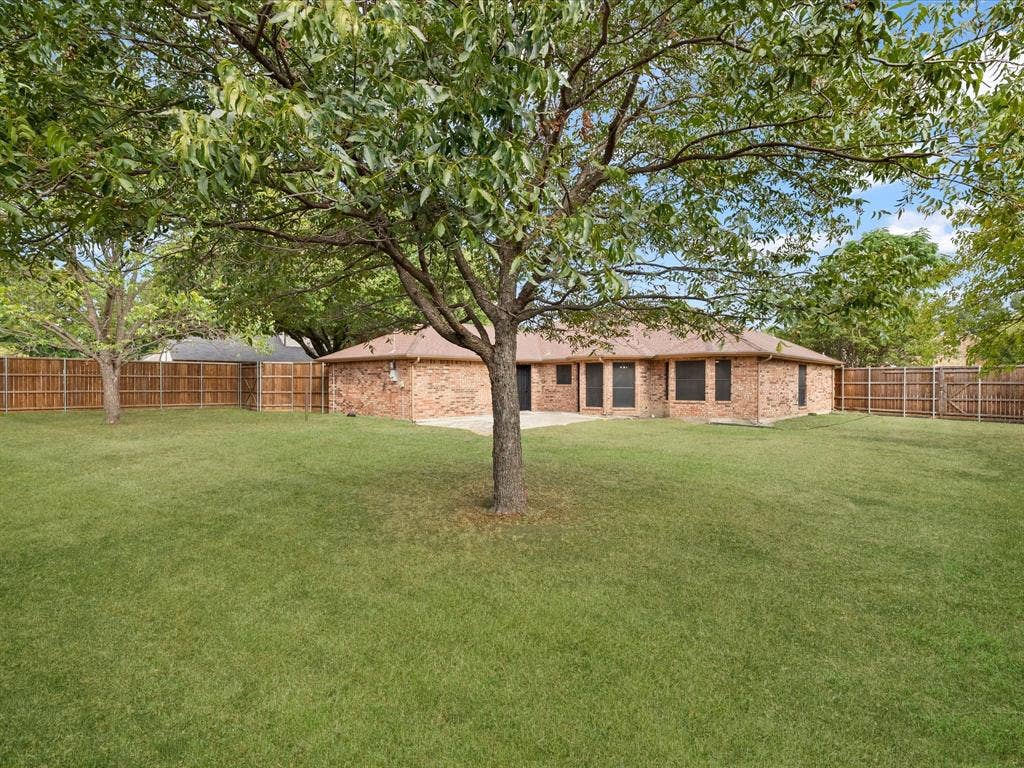 Expansive lawn with mature trees, a full privacy fence, and a brick-faced exterior